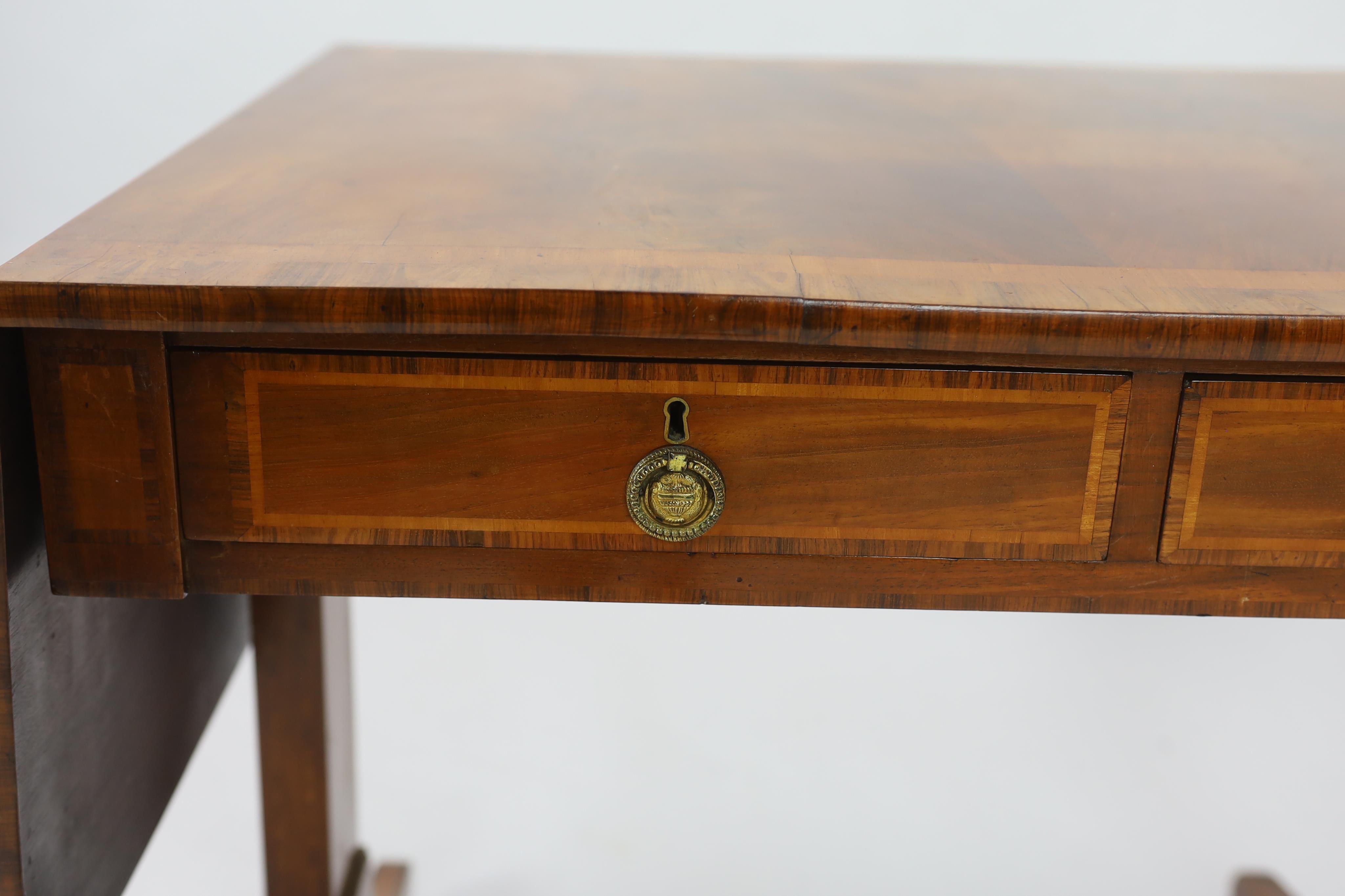 A Regency satinwood banded mahogany sofa table, with two frieze drawers on end standards with turned stretcher and downswept legs, fitted brass castors, width 80cm, depth 64cm, height 71cm. Condition - fair